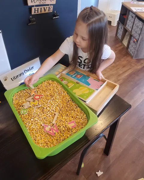 A girl scooping in a bin of dried corn with small cups