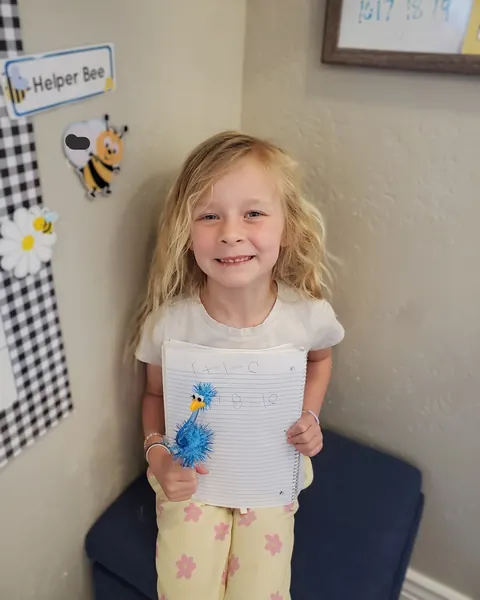 A smiling preschool girl holding up her notebook and a marker